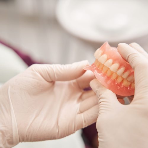 Cropped view of the dentist holding dentures in her hands. Dental prosthesis in the hands of the doctor close-up. Front view of complete denture. Dentistry conceptual photo. Prosthetic dentistry. False teeth